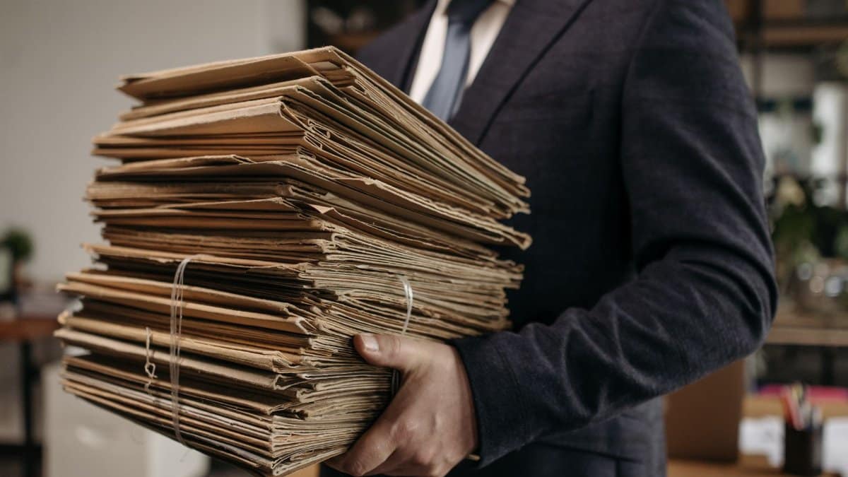Close-up of business professional holding a large stack of brown folders in an office setting.