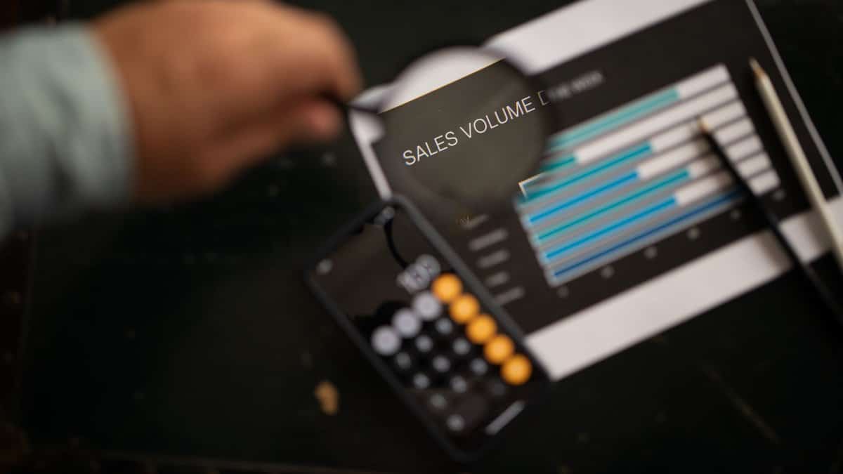 A focused examination of sales volume data using a magnifying glass and calculator.