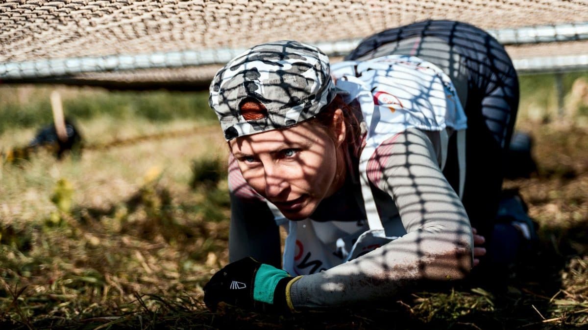 A young woman crawls under a net in an outdoor training or obstacle course.