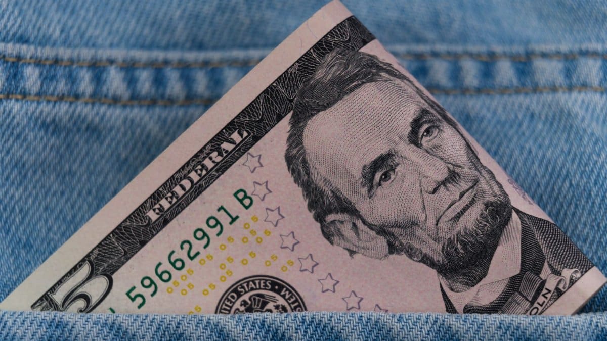 A five dollar bill tucked into a blue denim jeans pocket, symbolizing savings or cash on the go.