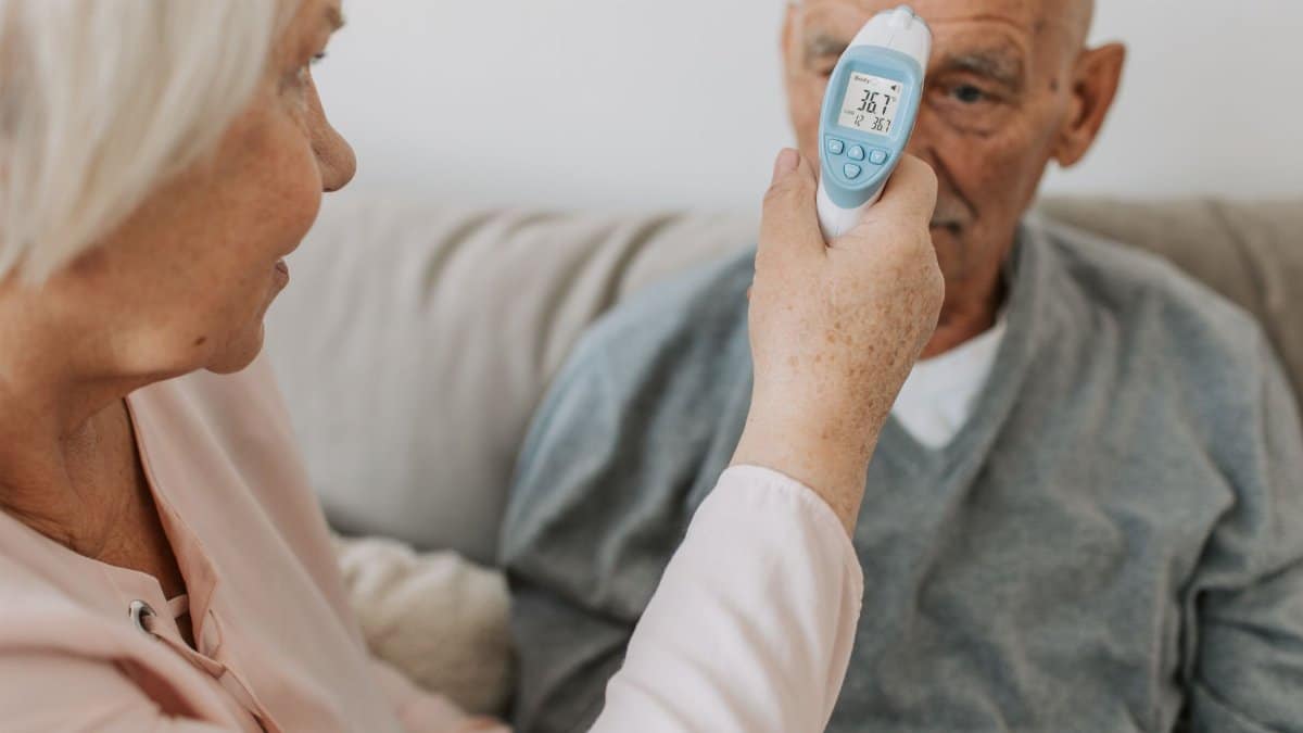An elderly woman checks the temperature of a senior man using a digital thermometer indoors.