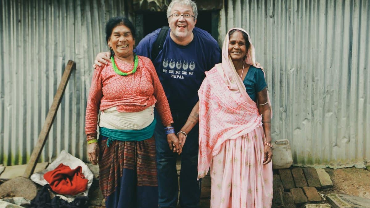 A joyful group portrait of diverse individuals standing and smiling outdoors in a rural setting.