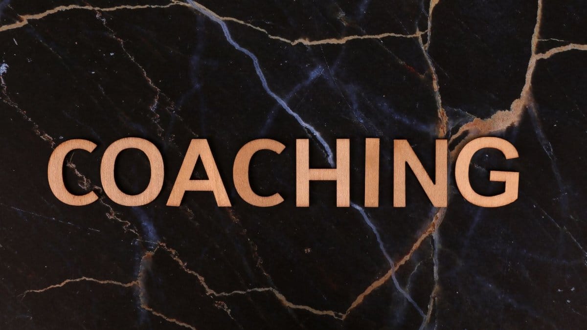 Wooden letters spelling 'Coaching' on dark marble surface, emphasizing guidance and mentorship.