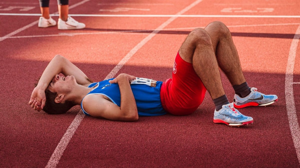 A tired athlete lies on the track, recovering after a race in sportswear.