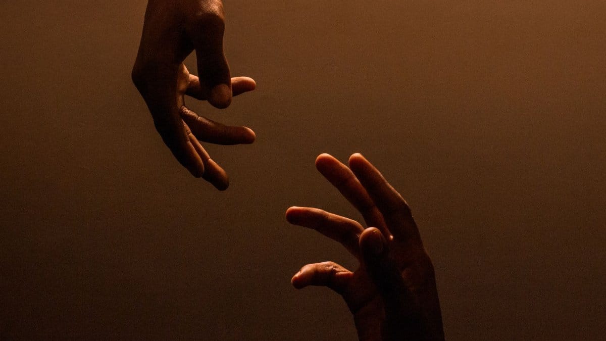 Two hands reaching towards each other against a dark, warm background, symbolizing connection.