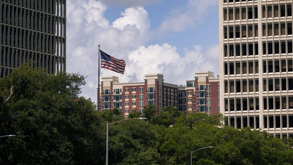 American flag waving between Houston skyscrapers on a sunny day.