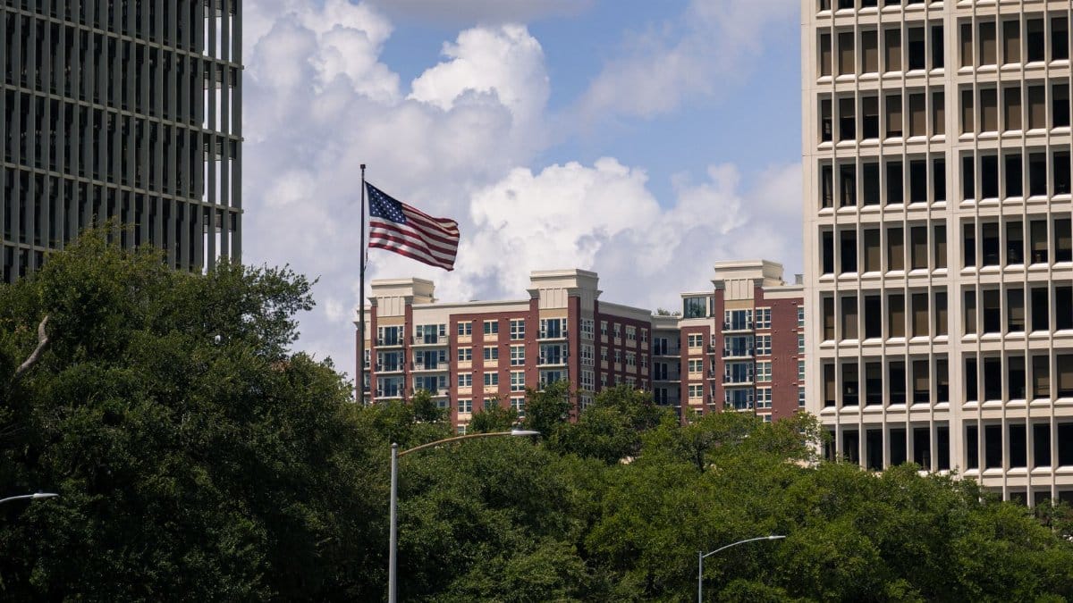 American flag waving between Houston skyscrapers on a sunny day.
