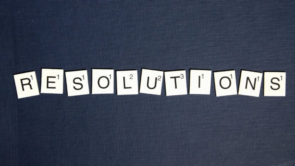Scrabble tiles spell 'RESOLUTIONS' on a textured dark blue background, capturing a New Year theme.