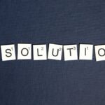 Scrabble tiles spell 'RESOLUTIONS' on a textured dark blue background, capturing a New Year theme.