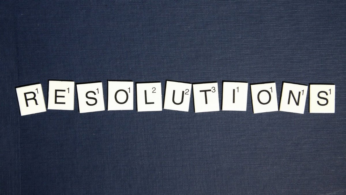 Scrabble tiles spell 'RESOLUTIONS' on a textured dark blue background, capturing a New Year theme.