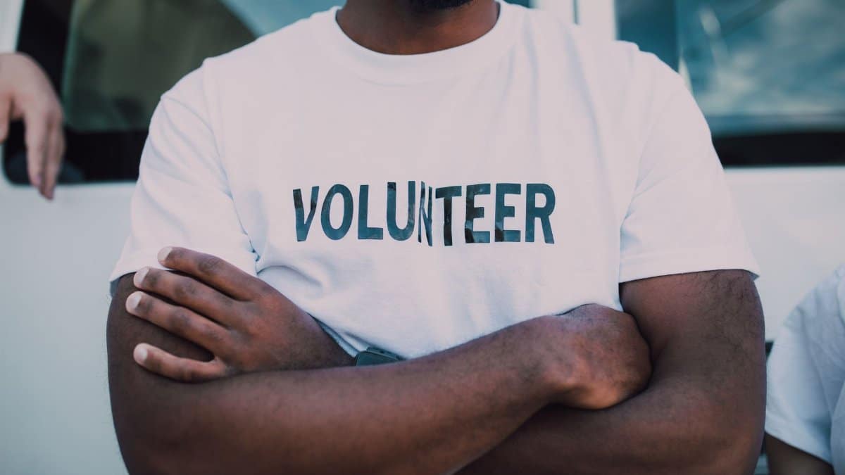 A close-up of a person wearing a volunteer shirt with arms crossed, promoting community service.