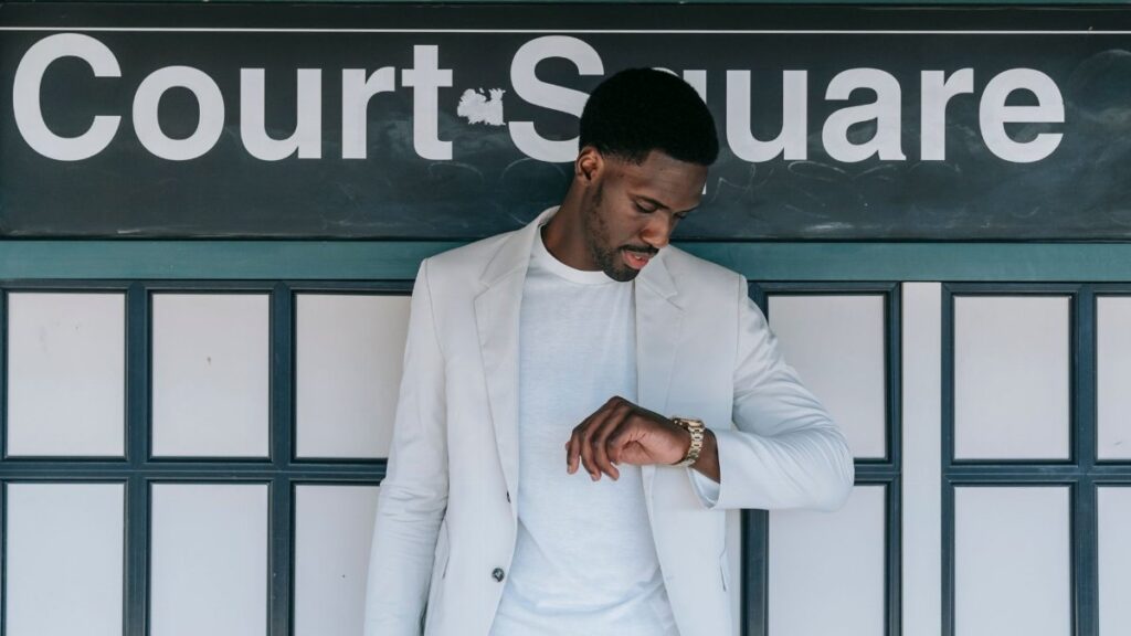 A fashionable man in a white blazer checks his wristwatch at Court Square station.