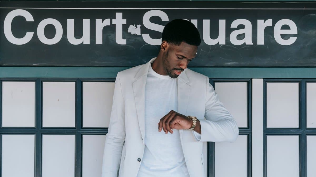 A fashionable man in a white blazer checks his wristwatch at Court Square station.