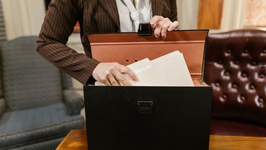 Close-up of a businesswoman organizing files in a black box in an office setting.