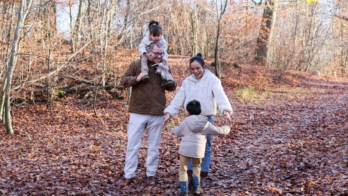 A family strolling through a forest during fall, surrounded by vivid autumn leaves.
