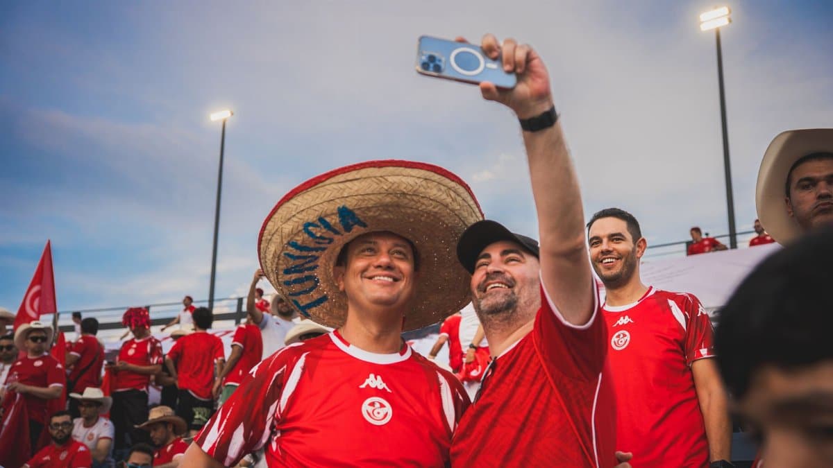 Cheerful soccer fans in red jerseys capture a selfie at a lively stadium event. Enthusiastic atmosphere.