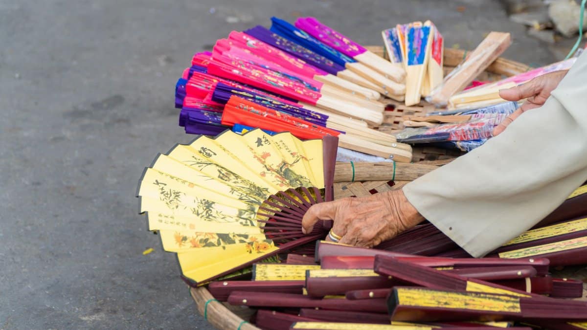 A close-up of a vendor showcasing handmade decorative fans on a street market.