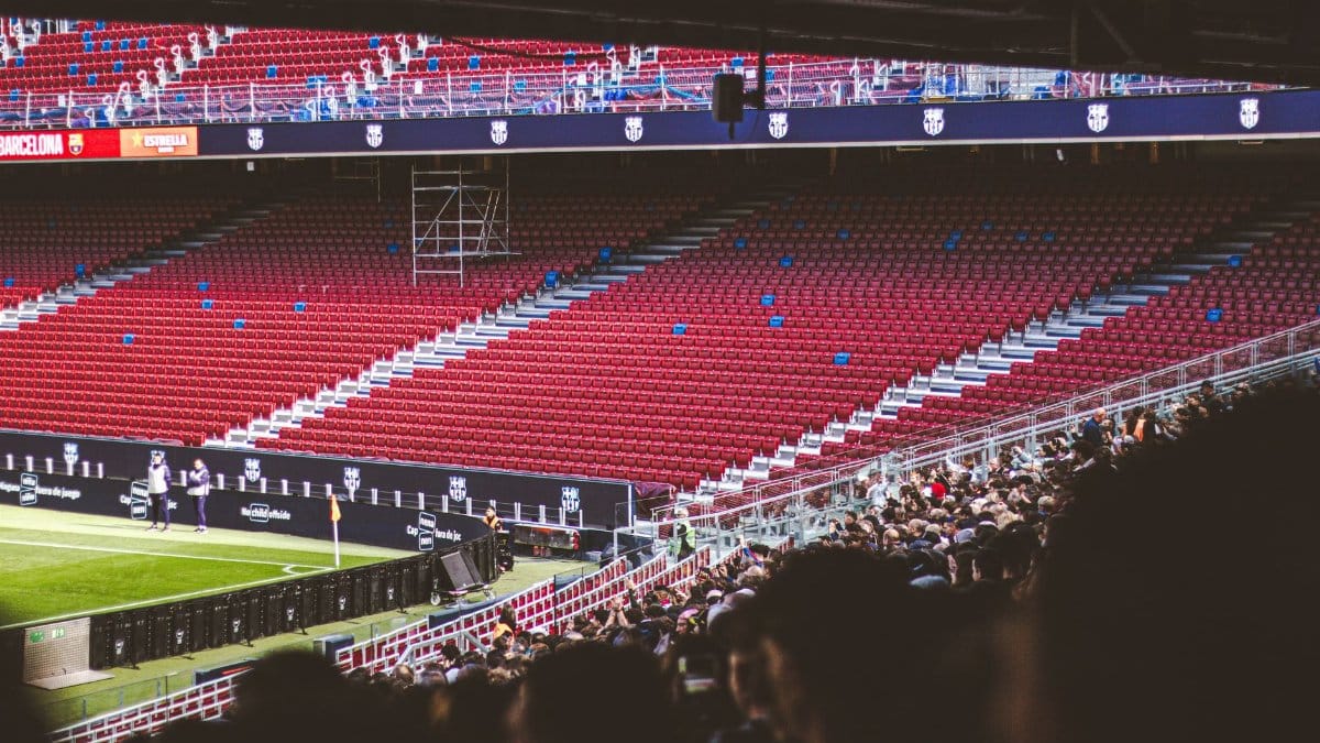 Panoramic view of stadium with empty red seats and crowd gathered for a live match.