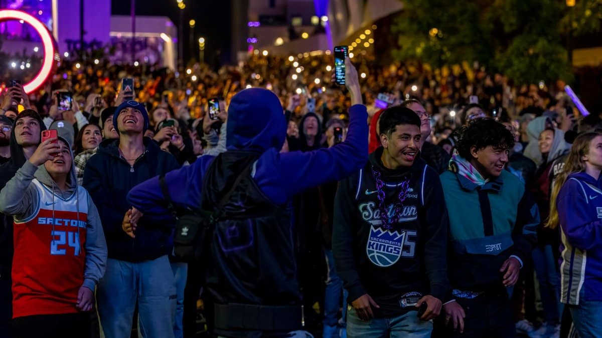 Vibrant crowd celebrating outdoors at night with lights and smartphones.