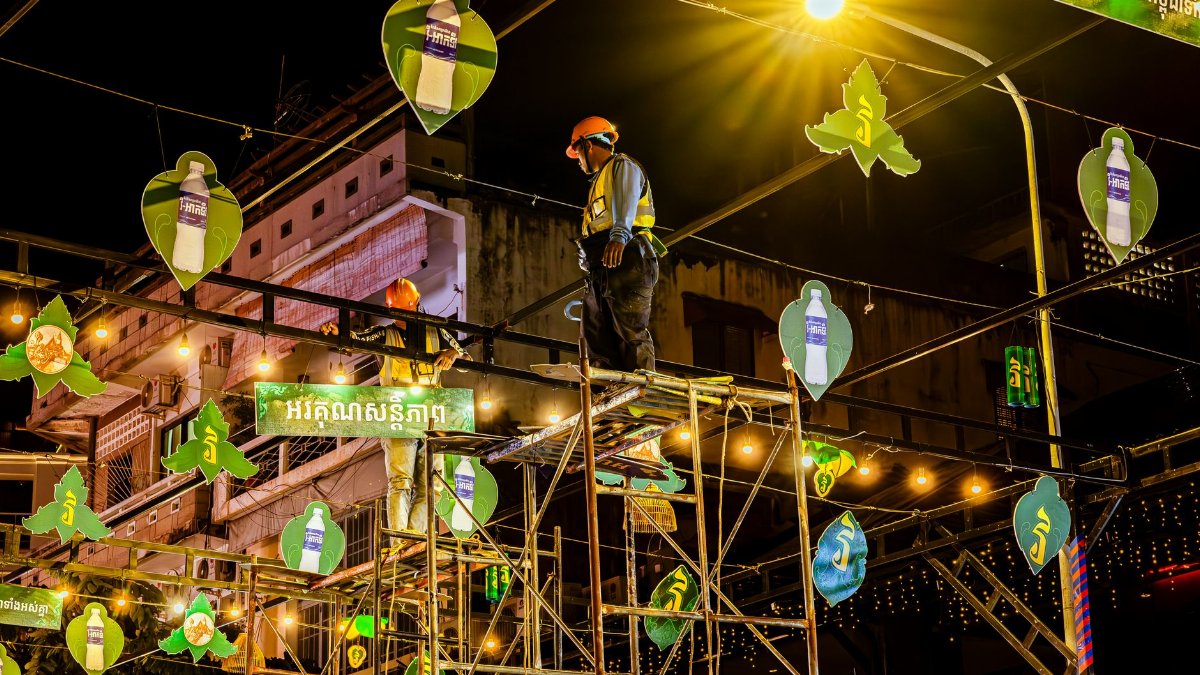 Workers installing decorative lights at night in an urban area, showcasing construction and festival preparations.