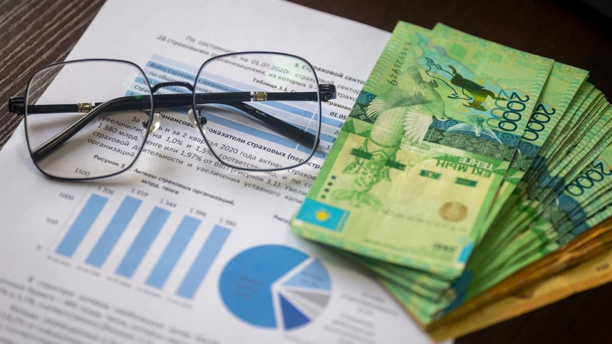 Kazakhstani tenge notes and financial reports on a desk, depicting financial analysis.