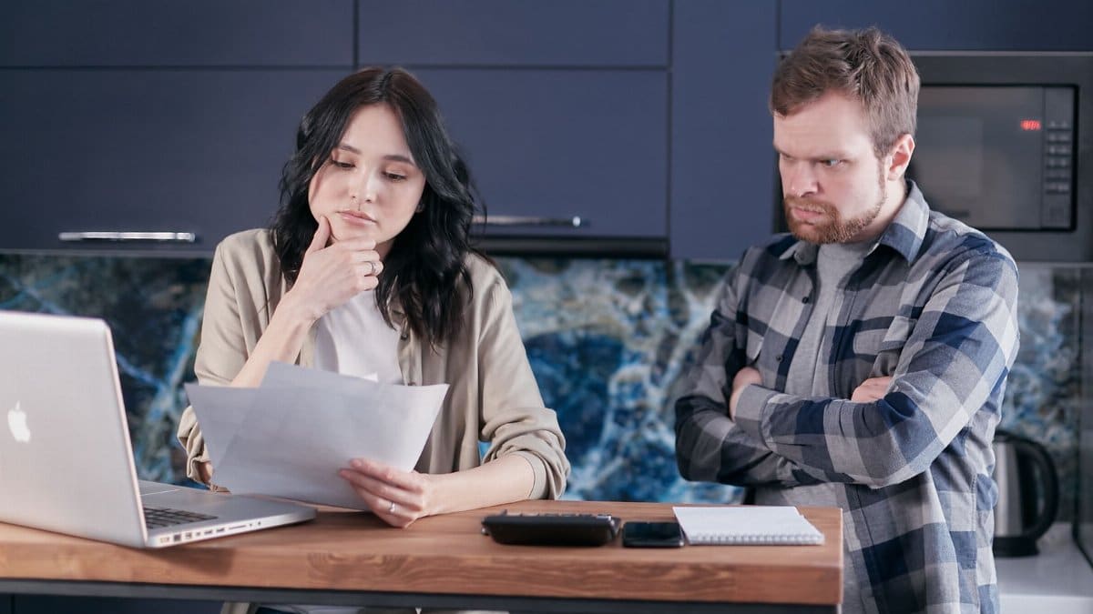 A couple sitting at a kitchen desk reviewing financial documents, using a laptop.