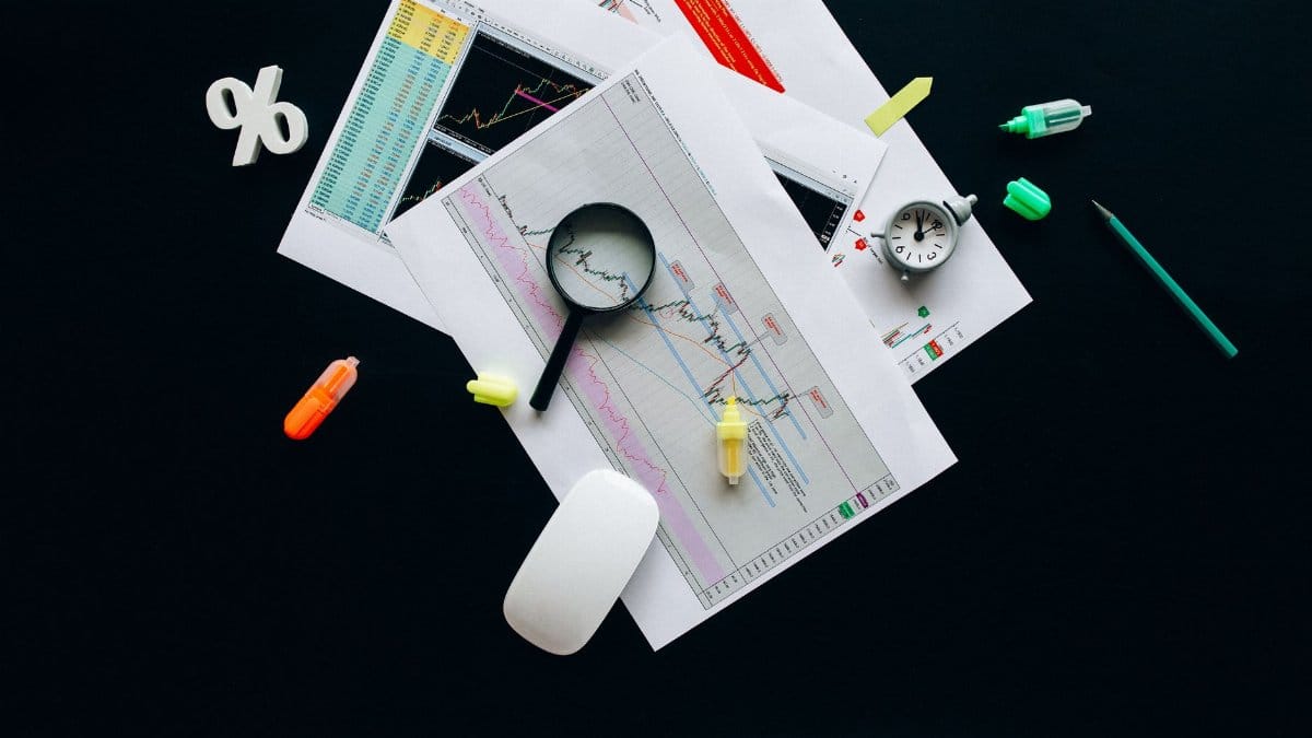 Overhead view of an office desk with financial documents, a magnifying glass, and stationery items, suggesting business analysis.