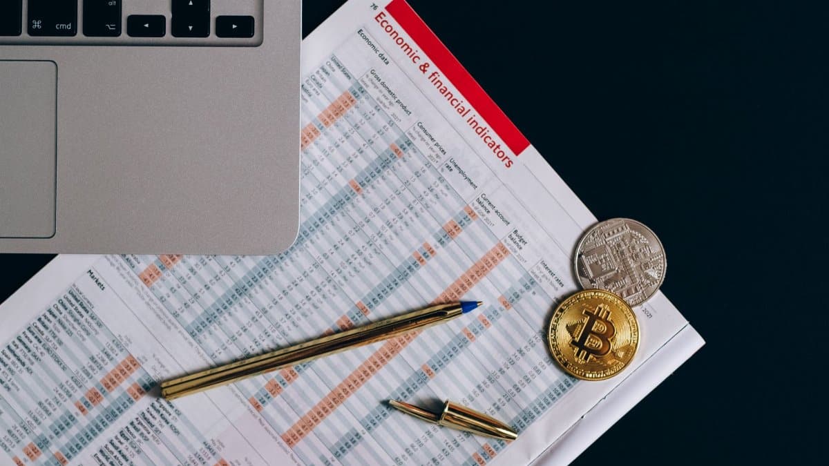 Top view of bitcoin coins on financial documents beside a laptop keyboard.