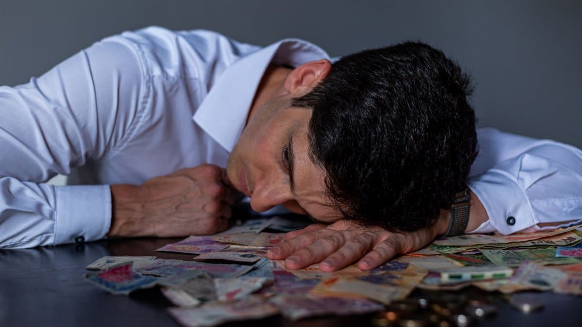 Man in stress resting on table covered with Argentine pesos symbolizing financial hardship.