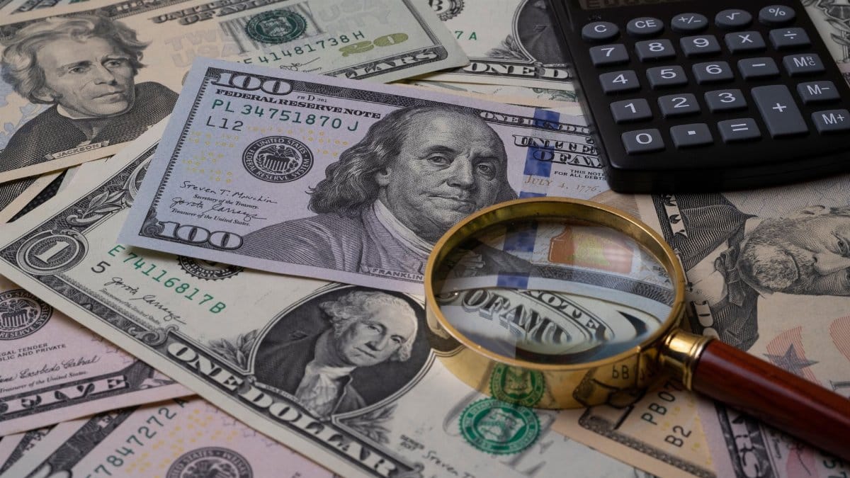 US currency bills with magnifying glass and calculator, symbolizing financial analysis.