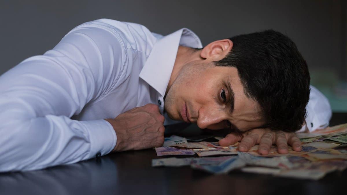 Adult man in white shirt resting on Argentine currency, showing financial stress.