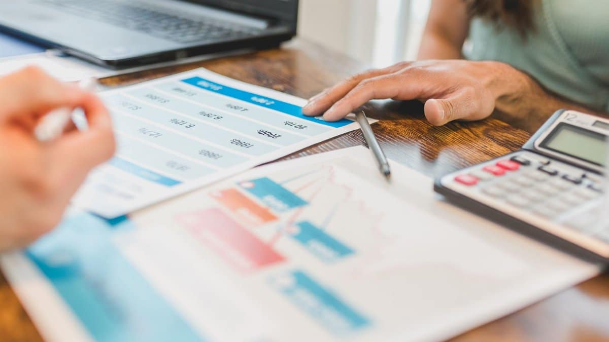 Hands at a desk with financial graphs, calculator, and pen, analyzing business data.