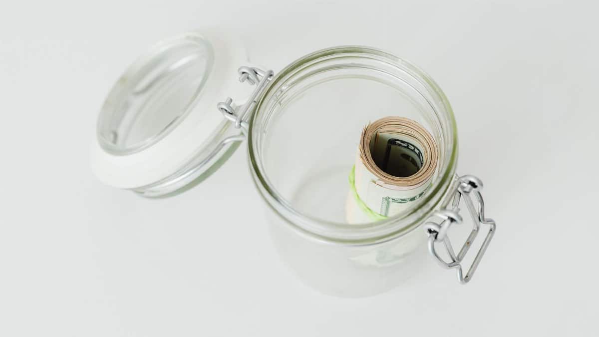 Close-up shot of rolled US dollar bills inside a glass jar on a white surface.