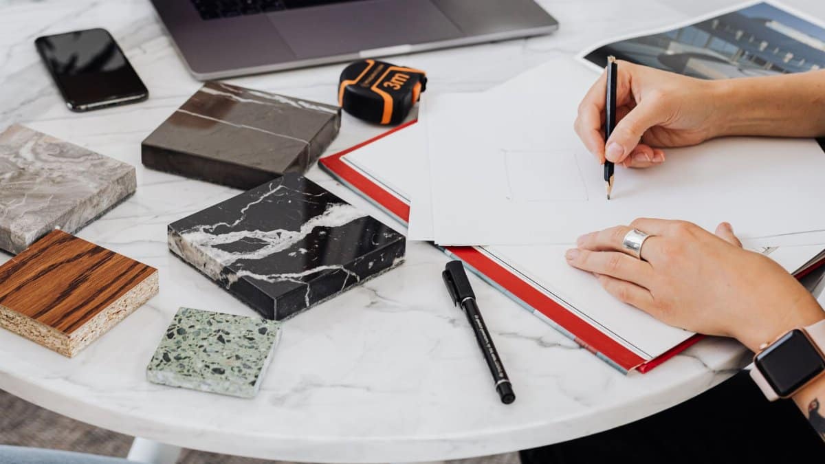 Architect works on design with material samples, sketching ideas on a marble table.