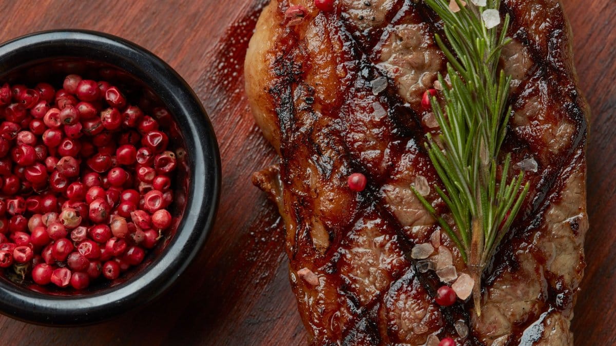 Close-up of grilled steak garnished with rosemary and pink peppercorns, enhancing its flavor.