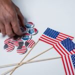 A hand reaches for voting buttons and American flags on a white background.