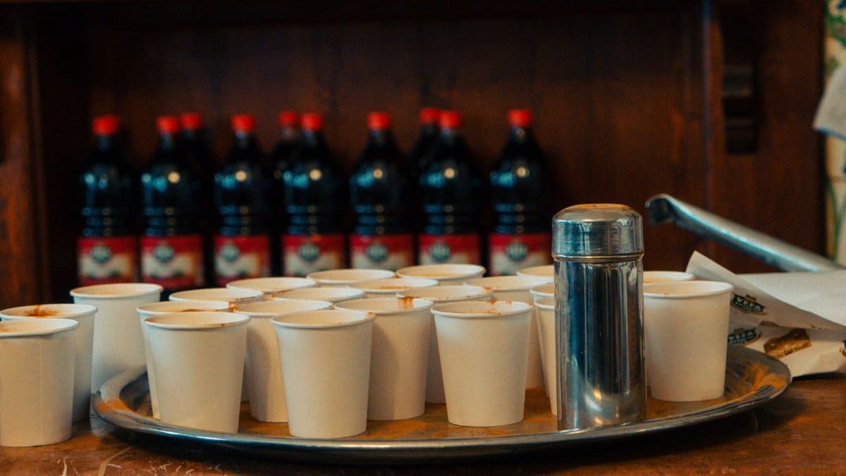 Tray of paper cups arranged on a cafe counter with drink bottles in background.