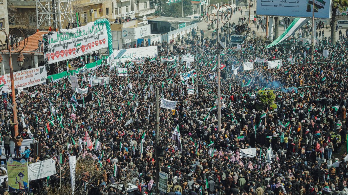Aerial view of a massive protest in Syria with banners and flags.