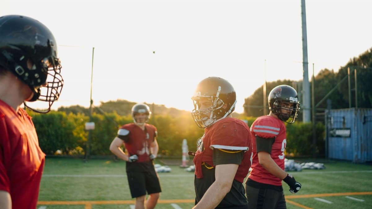 Football players practicing on a field at sunset, wearing gear and helmets.