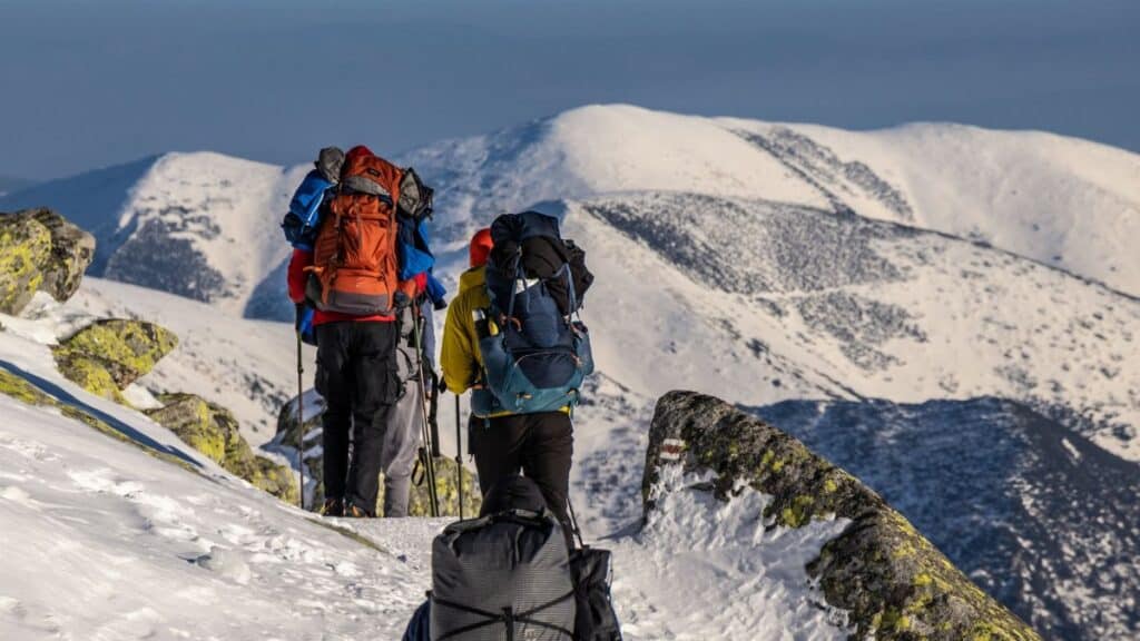 Adventurous hikers trek through a snowy mountain landscape with backpacks. Clear skies and rugged scenery.