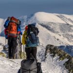 Adventurous hikers trek through a snowy mountain landscape with backpacks. Clear skies and rugged scenery.