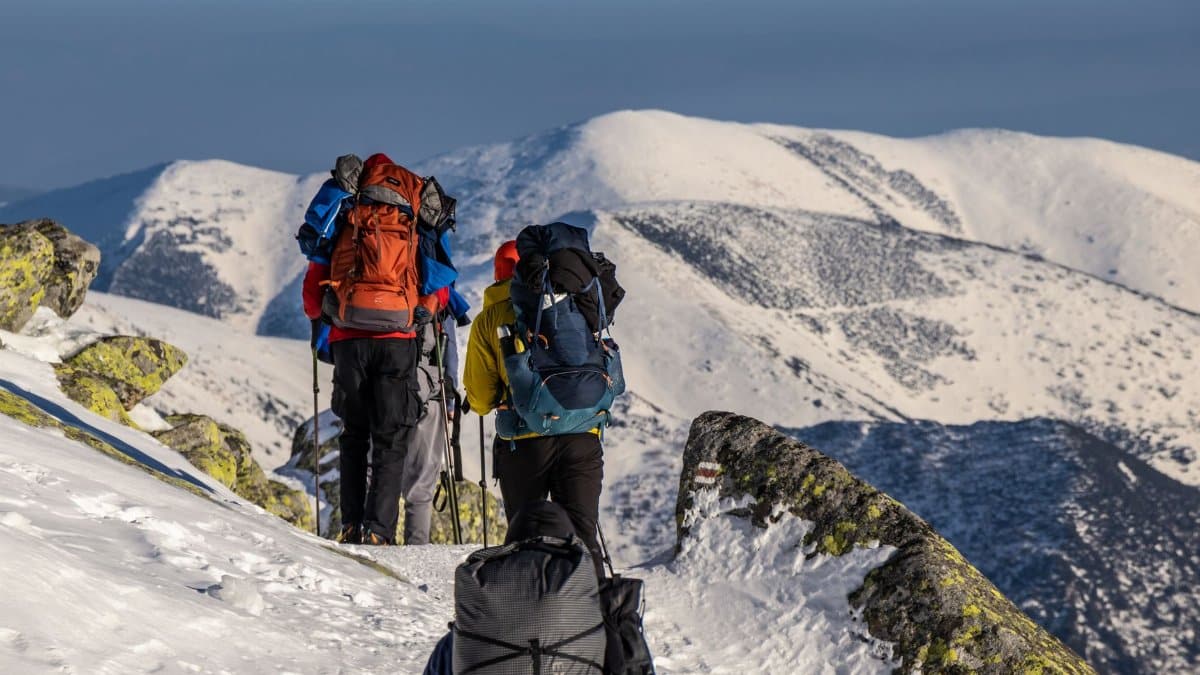 Adventurous hikers trek through a snowy mountain landscape with backpacks. Clear skies and rugged scenery.