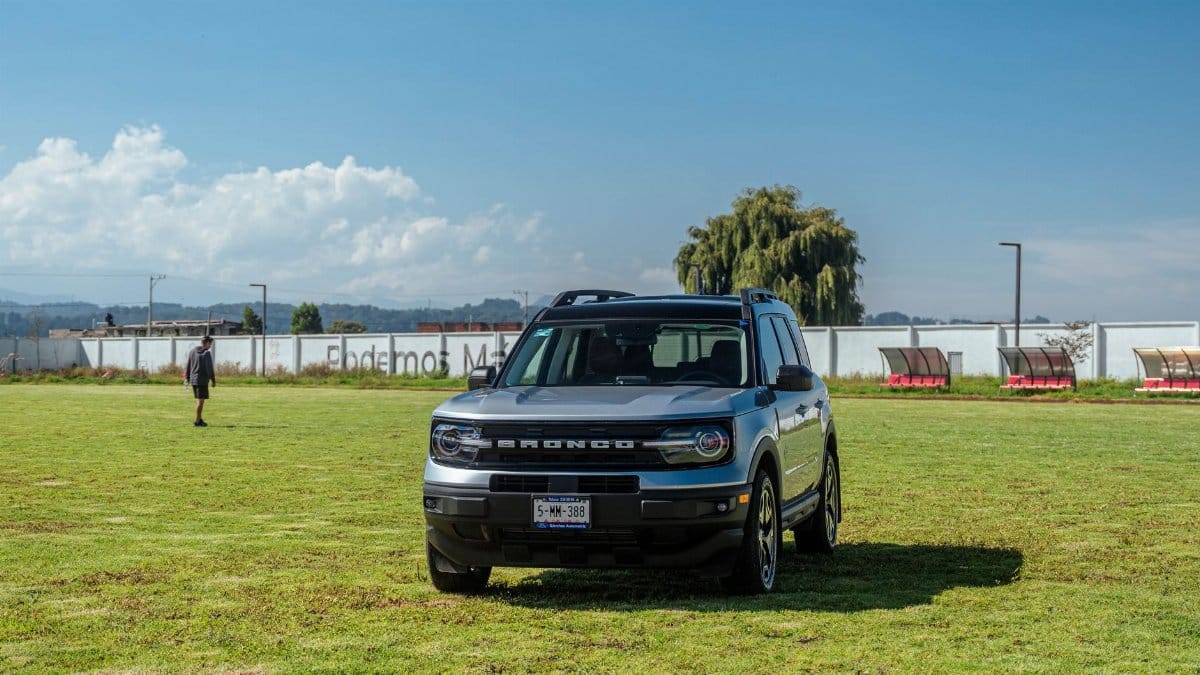 A silver Ford Bronco park on a grassy field under a blue sky, showcasing a rural landscape.