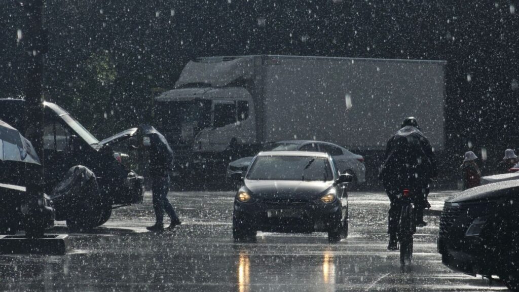 Moody urban street scene in heavy rain with cars and pedestrians.