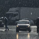 Moody urban street scene in heavy rain with cars and pedestrians.
