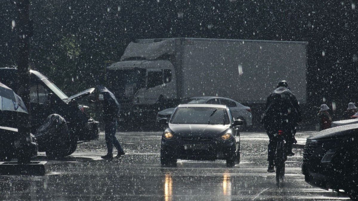 Moody urban street scene in heavy rain with cars and pedestrians.
