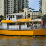 Yellow tour boat cruising Fort Lauderdale canal with high-rise buildings in view.