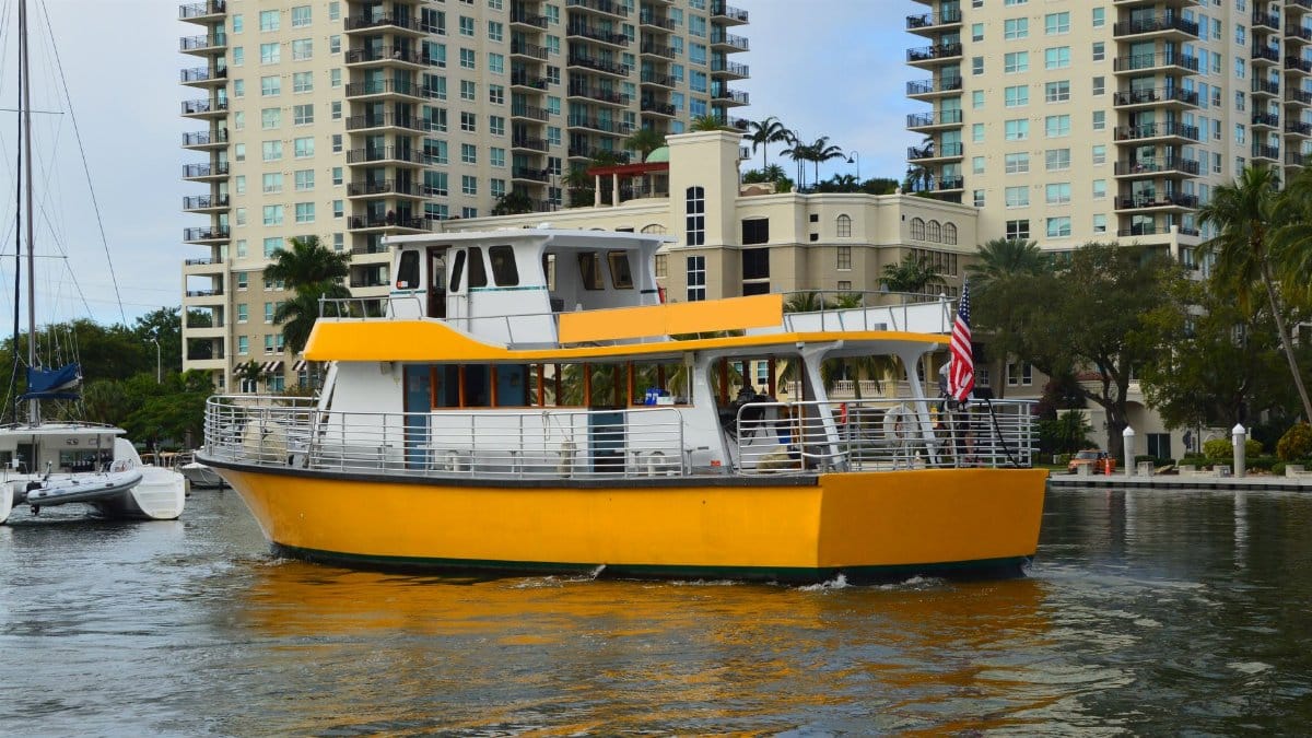 Yellow tour boat cruising Fort Lauderdale canal with high-rise buildings in view.