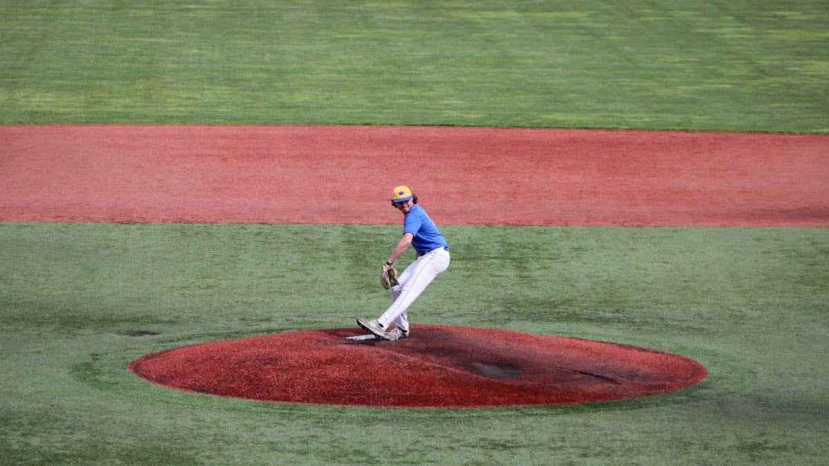 Teenage baseball pitcher throws a ball on an outdoor field, showcasing athletic skill.