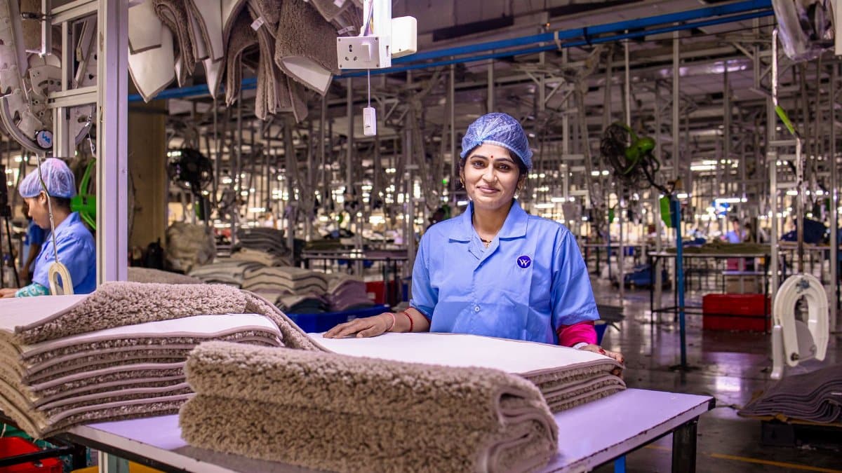 A female worker in a textile factory smiling, showcasing a stack of carpets.